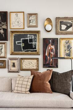 a living room filled with lots of framed pictures on the wall above a white couch