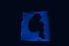 the silhouette of a person sitting in front of a blue light on a black background