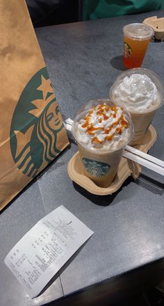 two drinks are sitting on a table with paper bags and papers next to each other