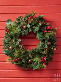 a christmas wreath hanging on the side of a red wall with holly berries and pine cones