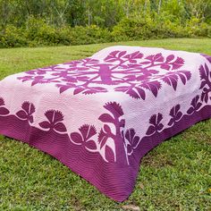 a purple and white quilt sitting on top of a lush green field