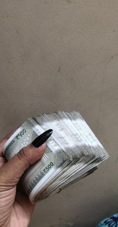 a person holding stacks of money in their left hand and a black pen sticking out of it