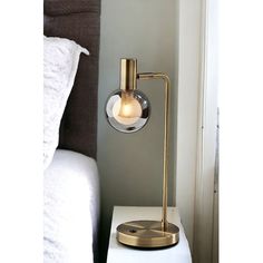 a lamp that is sitting on top of a white table next to a bed with pillows