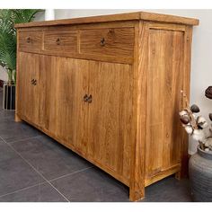 a large wooden dresser sitting on top of a tiled floor next to a potted plant