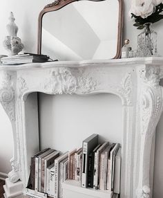 a white fireplace mantle with books on it and a mirror over the mantel above