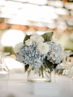 a glass vase filled with blue and white flowers on top of a table next to glasses