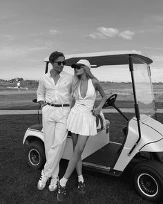 black and white photograph of two people in golf attire posing for the camera while sitting on a golf cart