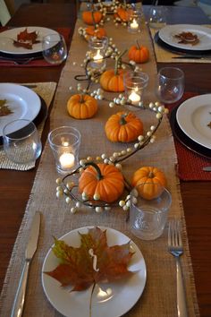 the table is set for thanksgiving dinner with pumpkins and leaves on it, along with candles