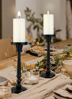 two candles are sitting on a table with plates and utensils