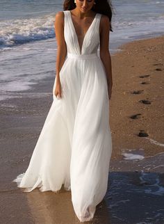 a woman in a white dress walking on the beach