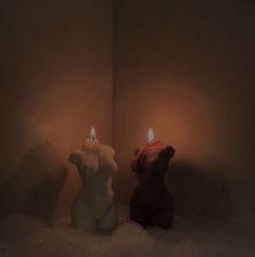 two lit candles sitting next to each other in a room with snow on the floor