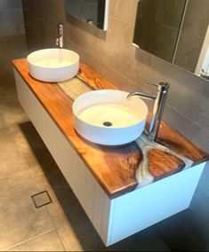 two white bowls are sitting on a wooden counter top in a modern bathroom with gray tile walls