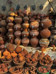 many clay pots are stacked on top of each other in front of a wall full of them