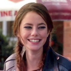 a woman with braids smiling and wearing a leather jacket in front of a building