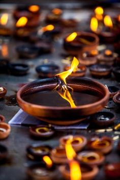 a table topped with lots of lit candles and bowls filled with liquid on top of it