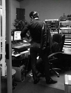 a man standing in front of a computer desk next to a keyboard and monitor screen