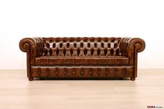 a brown leather couch sitting on top of a hard wood floor next to a white wall