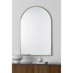 an arched mirror on top of a wooden dresser next to a white vase and lamp