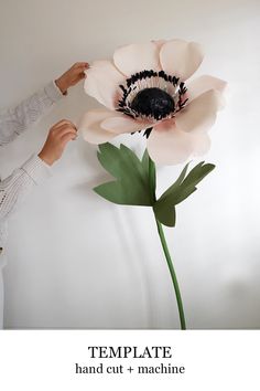 a woman is making a flower out of paper and glue on the wall with her hands