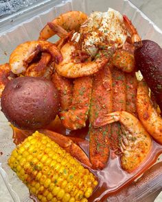 a plastic container filled with seafood and corn on the cob next to potato wedges