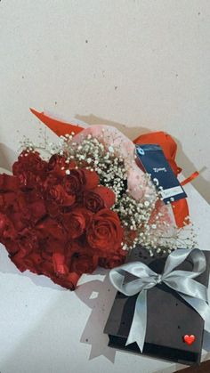 a bouquet of red roses and baby's breath sits next to a gift box