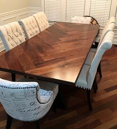 a dining room table and chairs with white upholstered backrests on wooden flooring