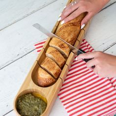 a person cutting bread in a wooden box on top of a red and white striped napkin