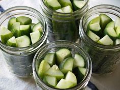 four jars filled with cucumbers sitting on top of a table