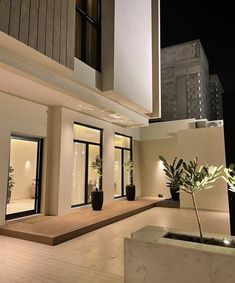 an outdoor area with potted plants and lights on the side of the building at night