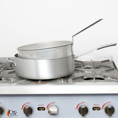 a silver pot sitting on top of a stove next to a frying pan with two tongs