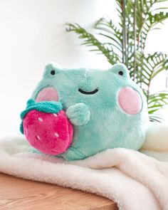 a green stuffed animal with a pink strawberry on it's back sitting on a white blanket