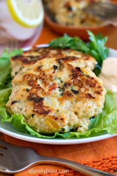 a crab cake with lettuce and lemon wedges on a plate next to a fork