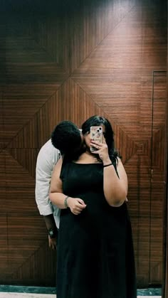 a man and woman standing in front of a wooden wall taking a selfie with their cell phone