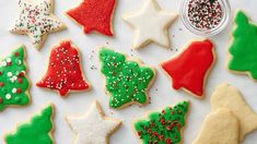 christmas cookies decorated with icing and sprinkles are arranged on a white surface