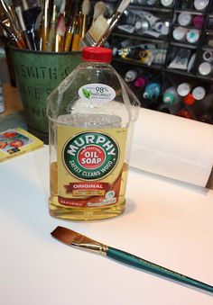 a bottle of soap sitting on top of a table next to paintbrushes and paints