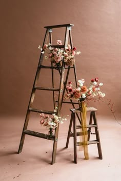 an old ladder with flowers on it next to a small wooden stool and vase filled with flowers