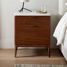 a nightstand with a lamp on top of it next to a bed