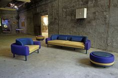 three couches and two chairs in an empty room with concrete walls on either side