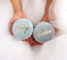 two bride's hands holding small personalized wedding badges with the word happily written on them