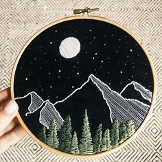 someone is holding up a small embroidery project with mountains and trees in the night sky