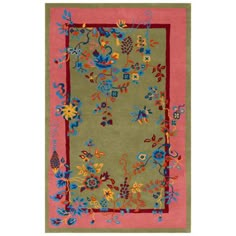 a green rug with colorful flowers and vines on the border, in front of a pink background