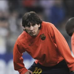 a man in an orange shirt is on the soccer field with his hands on his hips