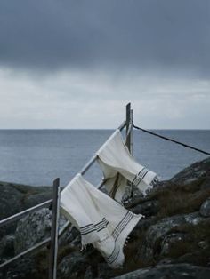 two cloths are hanging on the rocks by the water's edge, with dark clouds in the background