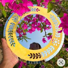 a hand holding up a yellow and blue paper plate with pink flowers in the background