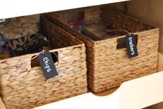 two wicker baskets with labels on them in a closet filled with food and snacks