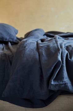 an unmade bed with dark blue sheets and pillows on top of the bedspread