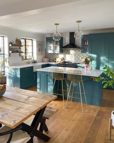 a kitchen with wooden floors and blue cabinets, an island table and stools in the center