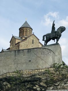 a statue of a man riding a horse on top of a stone wall with a church in the background