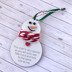 a snowman ornament hanging from a string on a white wooden background with a message