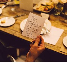 a person holding up a piece of paper with writing on it at a dinner table